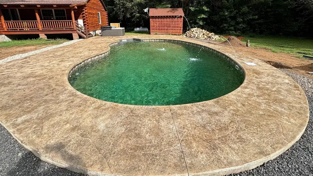 Stamped stone-pattern concrete deck curving around a kidney-shaped pool with a log cabin behind