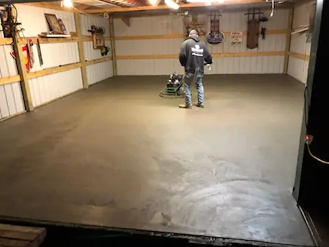 Finisher running a power trowel over a fresh concrete floor in a pole barn