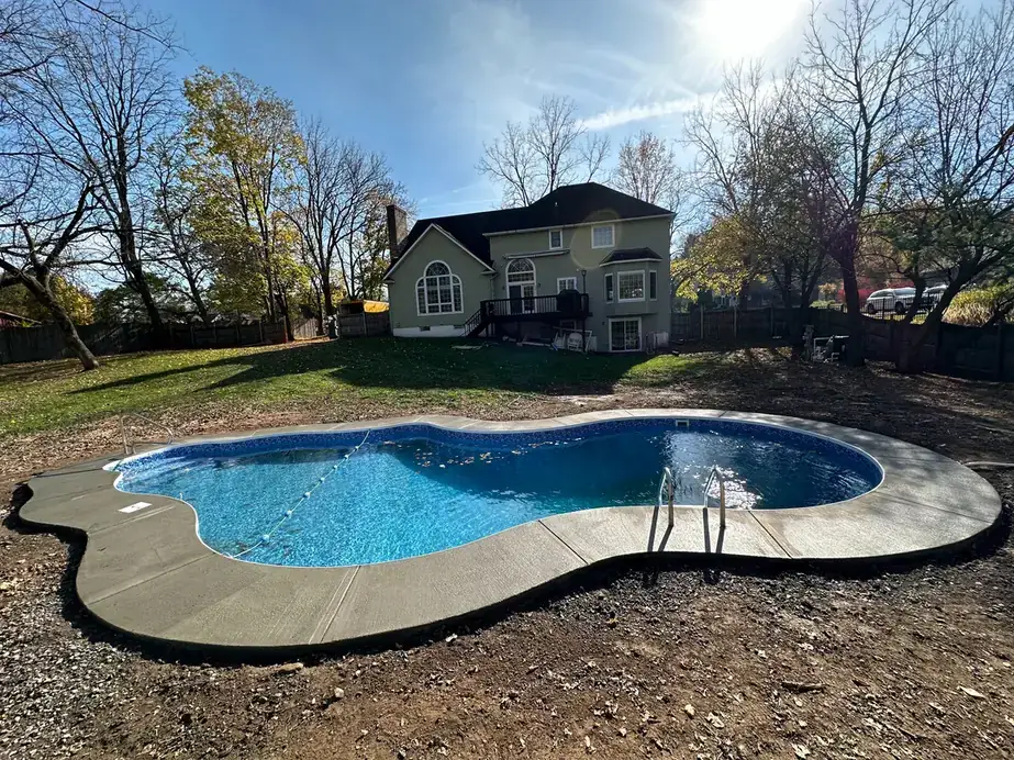 Grey concrete coping around a kidney-shaped pool behind a large colonial house