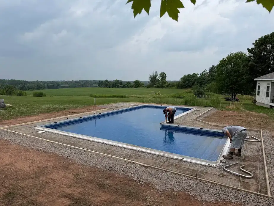 Crew setting a rectangular pool on a gravel base with the deck edge formed around it