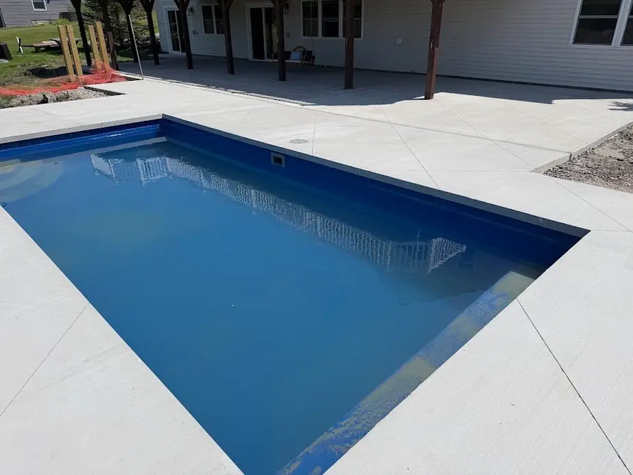 Light grey broom-finish concrete deck around a blue rectangular pool