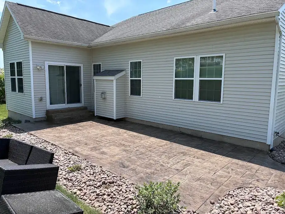 Stamped stone-pattern concrete patio along pale vinyl siding, river rock border